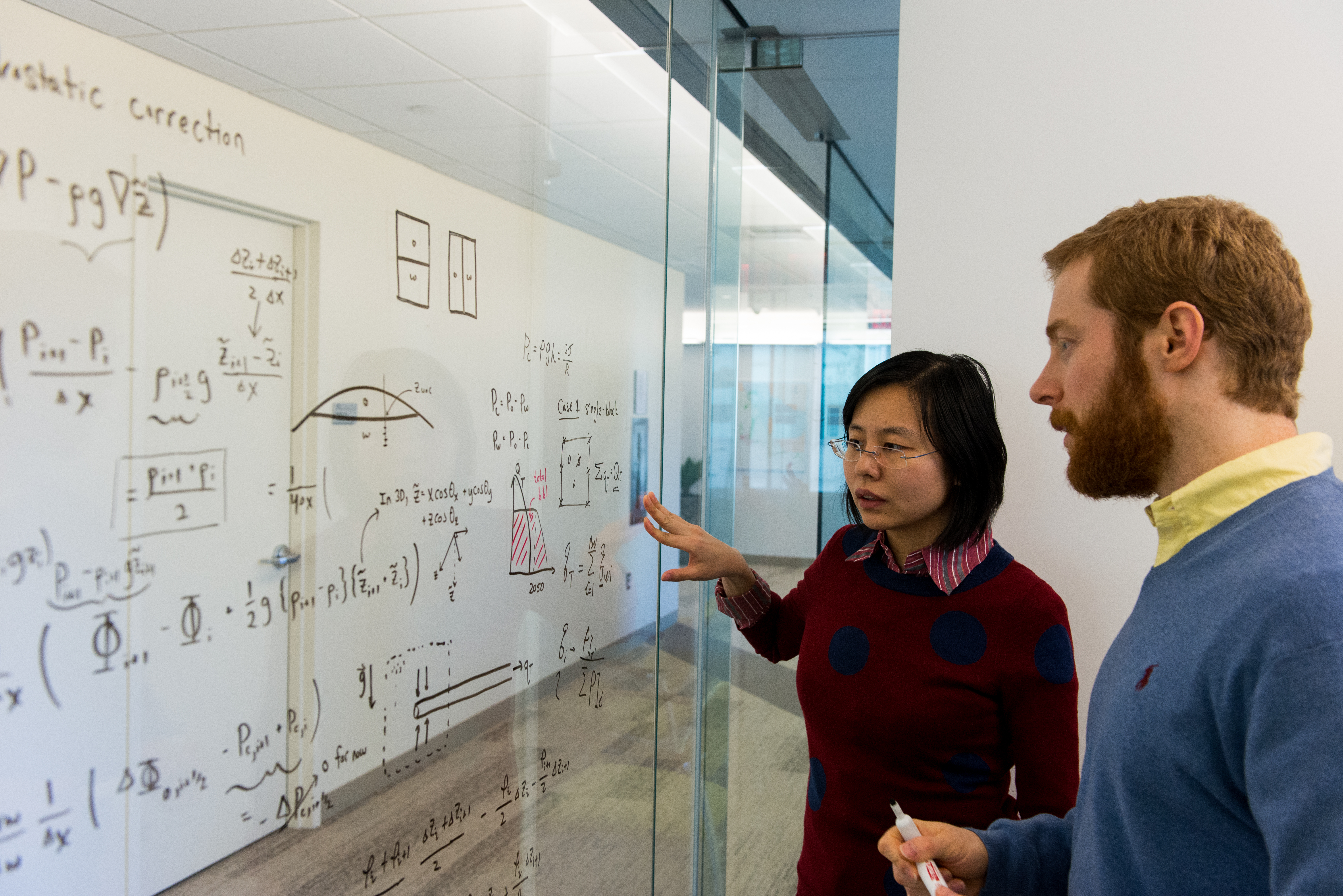 Male and female technicians view whiteboard calculations at our Boston technology research center