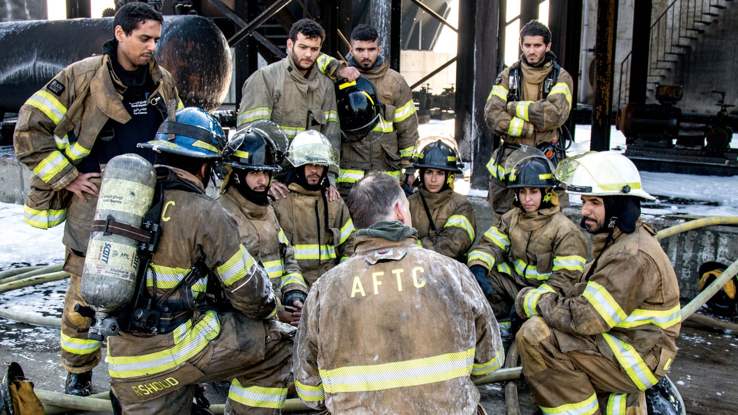 Group of trainee Saudi Aramco firefighters in protective clothing in a group discussion