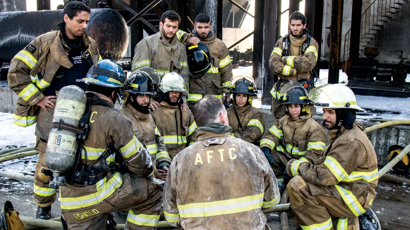 Group of trainee Saudi Aramco firefighters in protective clothing in a group discussion