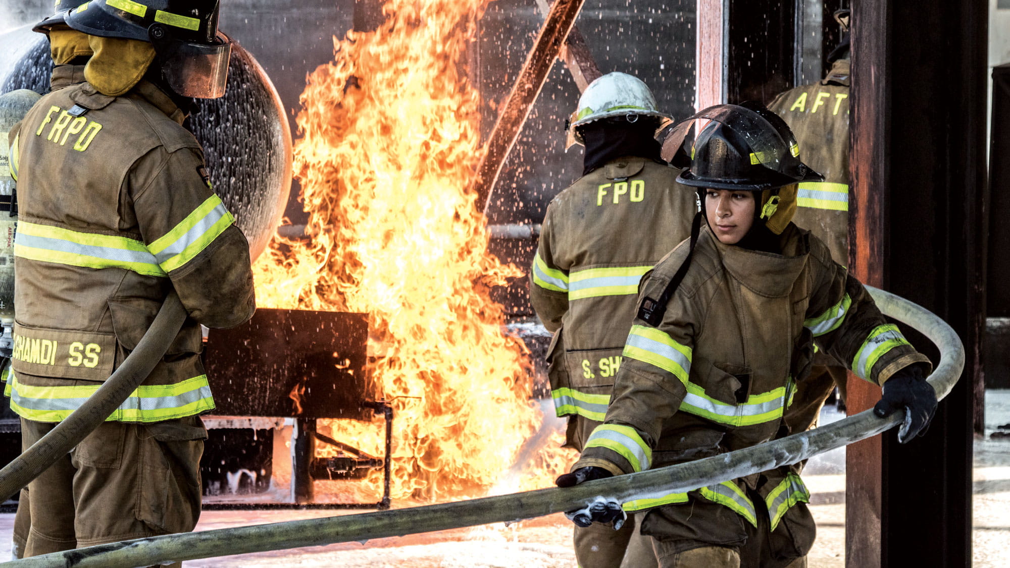 Female firefighter in protective clothing with a fire in the background