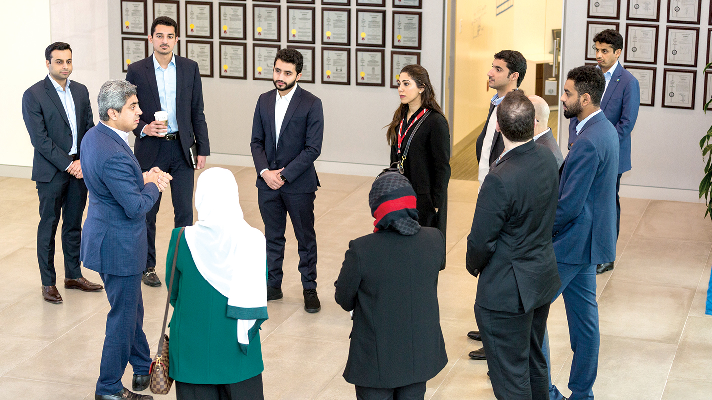 A group of YLAB attendees congregating in front of a wall with several pictures of patents awarded to Saudi Aramco