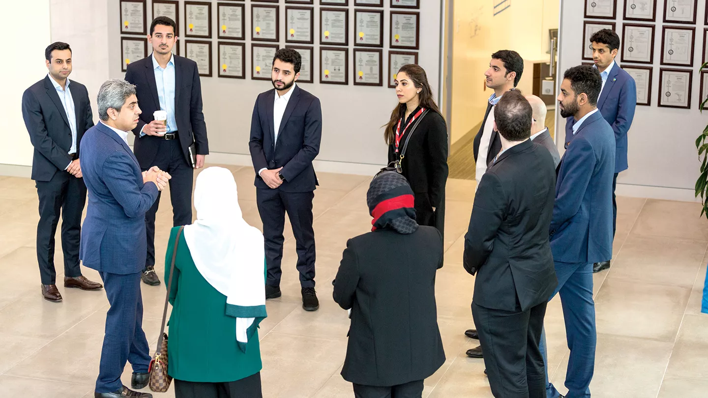 A group of YLAB attendees congregating in front of a wall with several pictures of patents awarded to Saudi Aramco